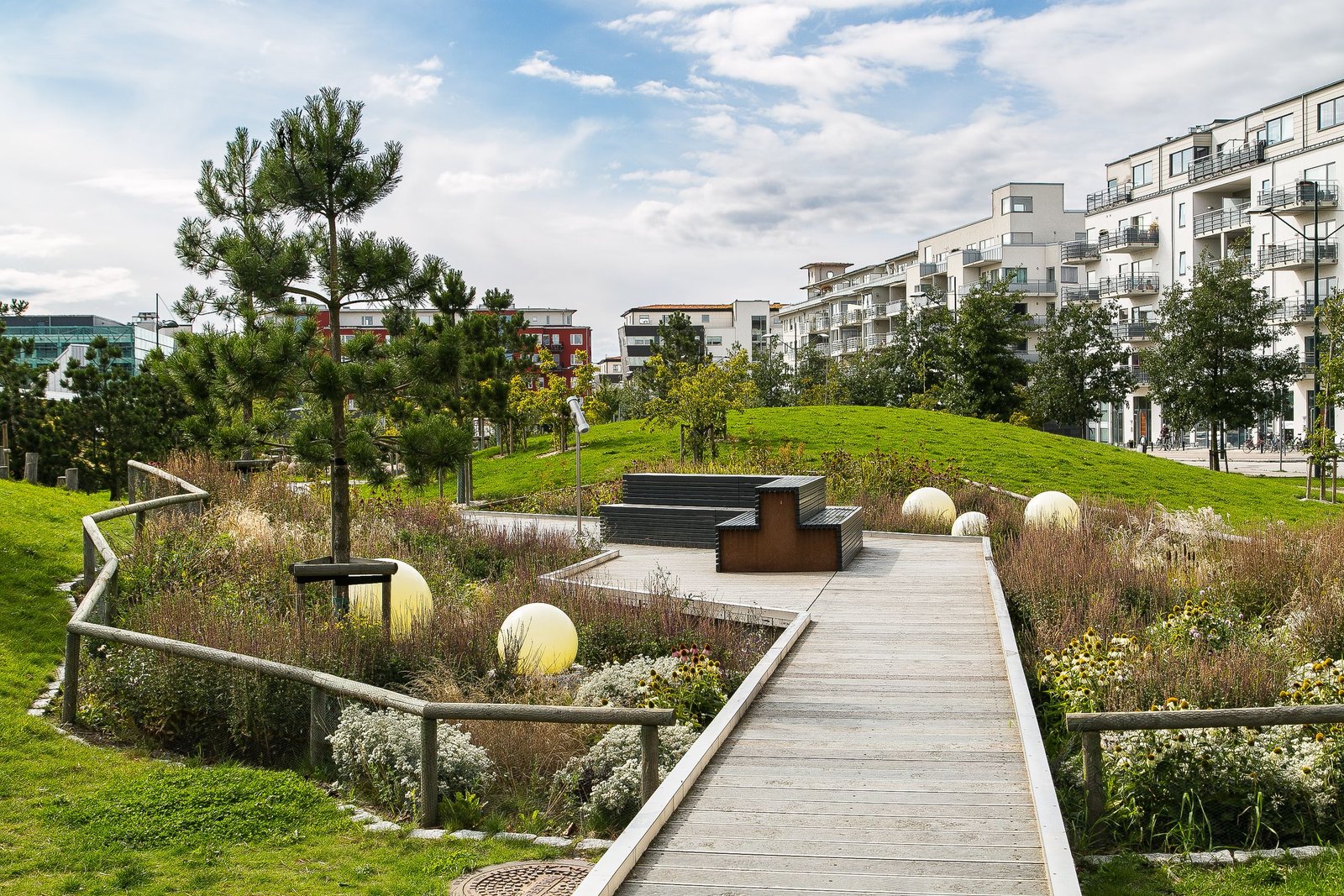 A scenic urban park featuring a wooden walkway, benches, and modern apartment buildings.